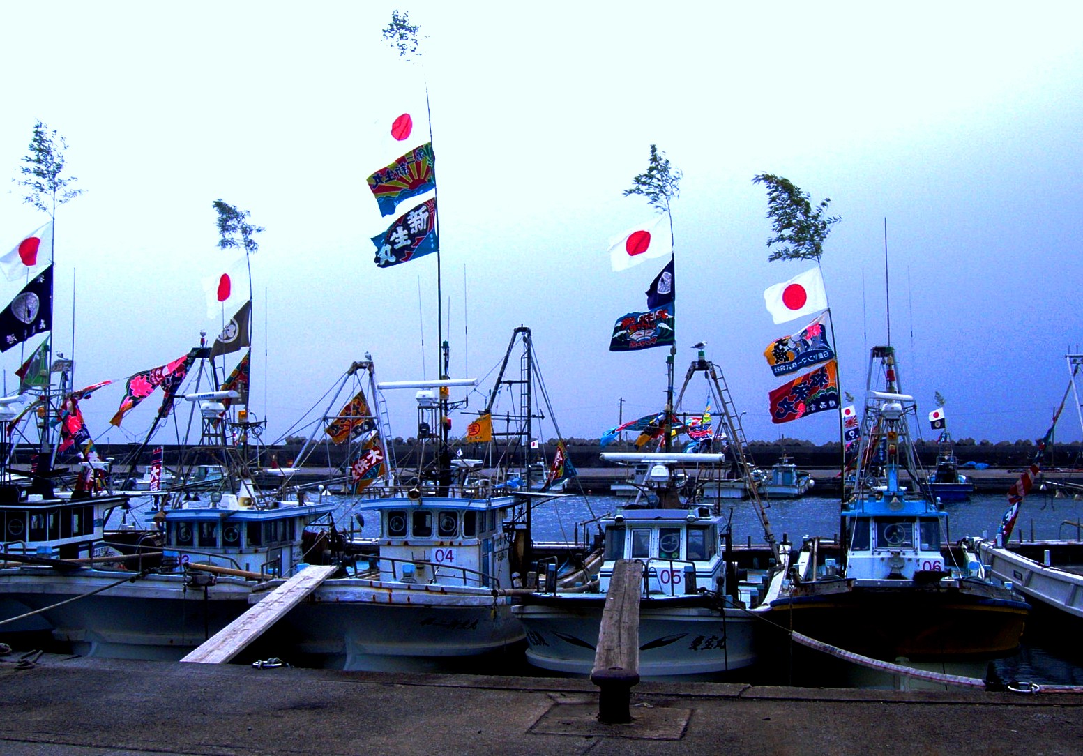 漁港に並ぶ大漁旗を立てた小型底曳網漁船