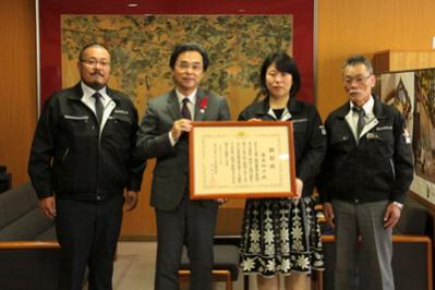 賞状を持つ永松市長と藤本さん、株式会社光伸電気工事の皆さんの写真